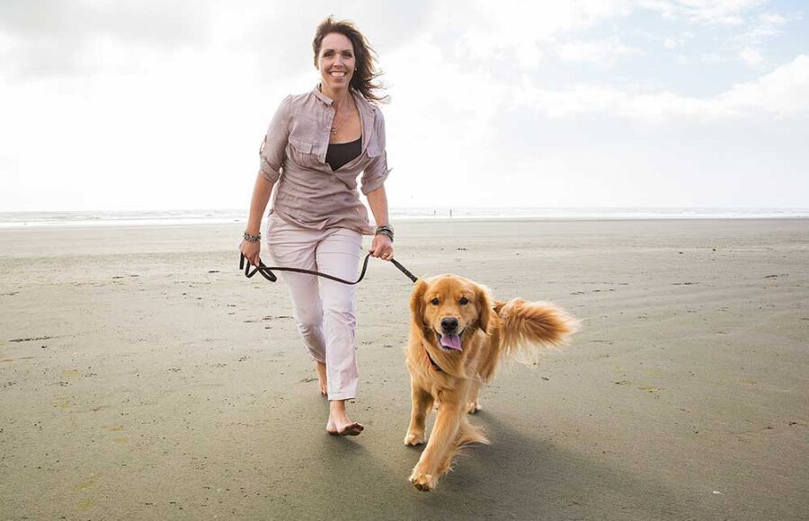 Adult Woman Walking A Golden Retriever Dog At The Beach